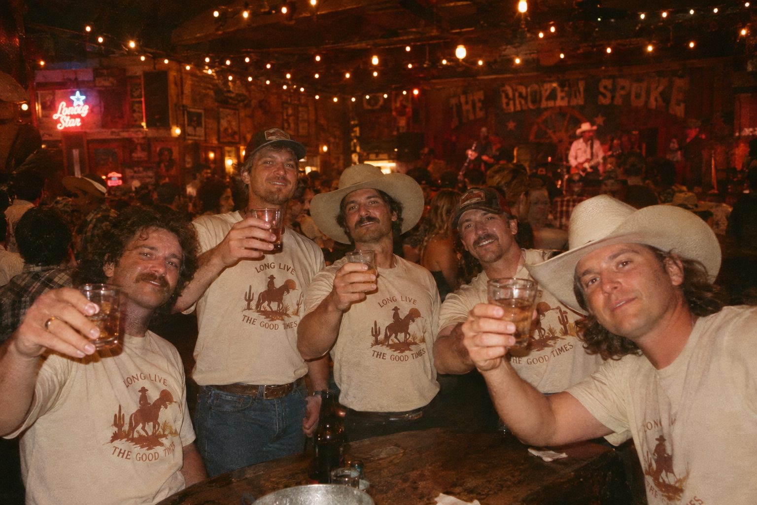 Groomsmen in cream western shirts raising glasses in a honky-tonk bar